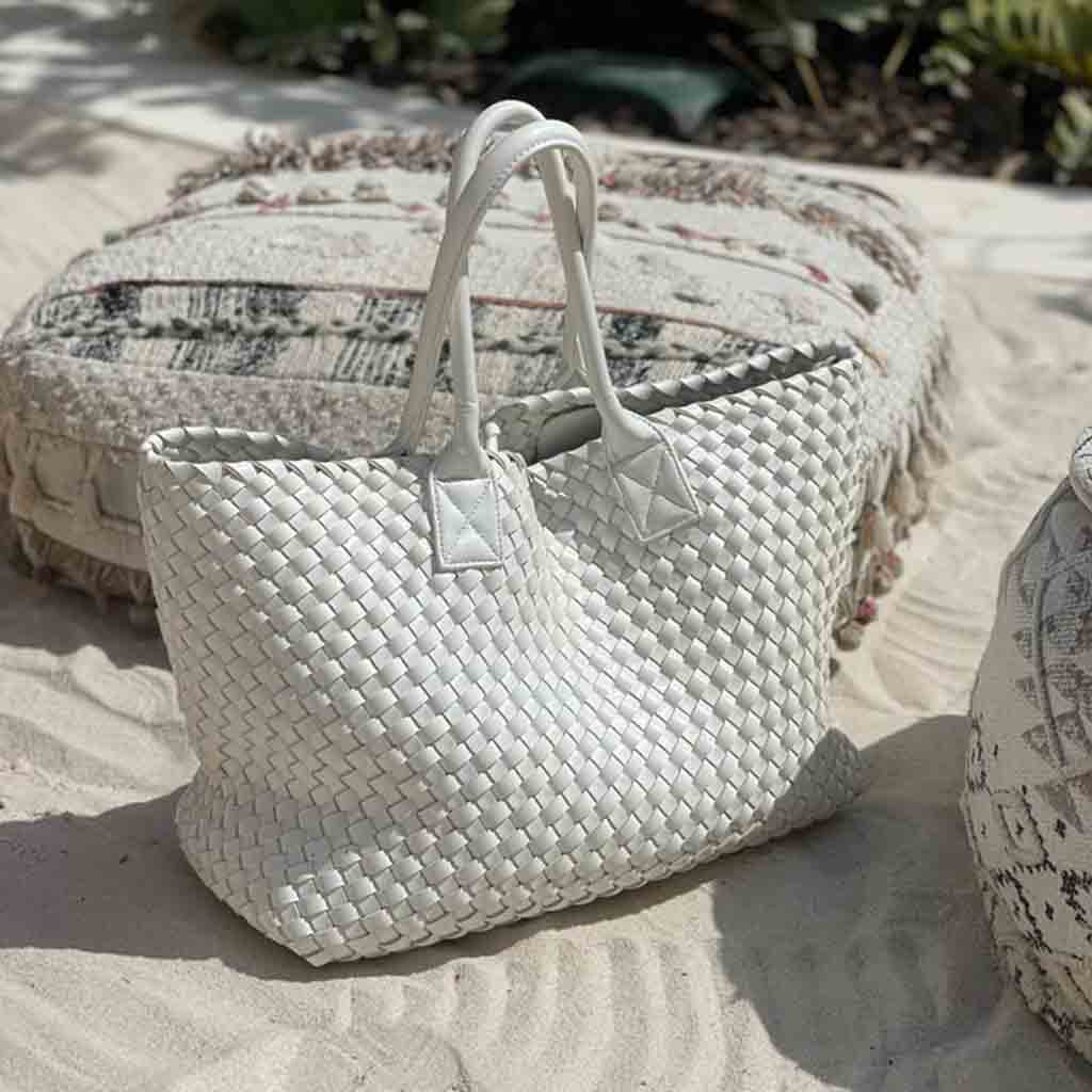 White hand woven Nicola handbag on a sandy surface with blurred natural background